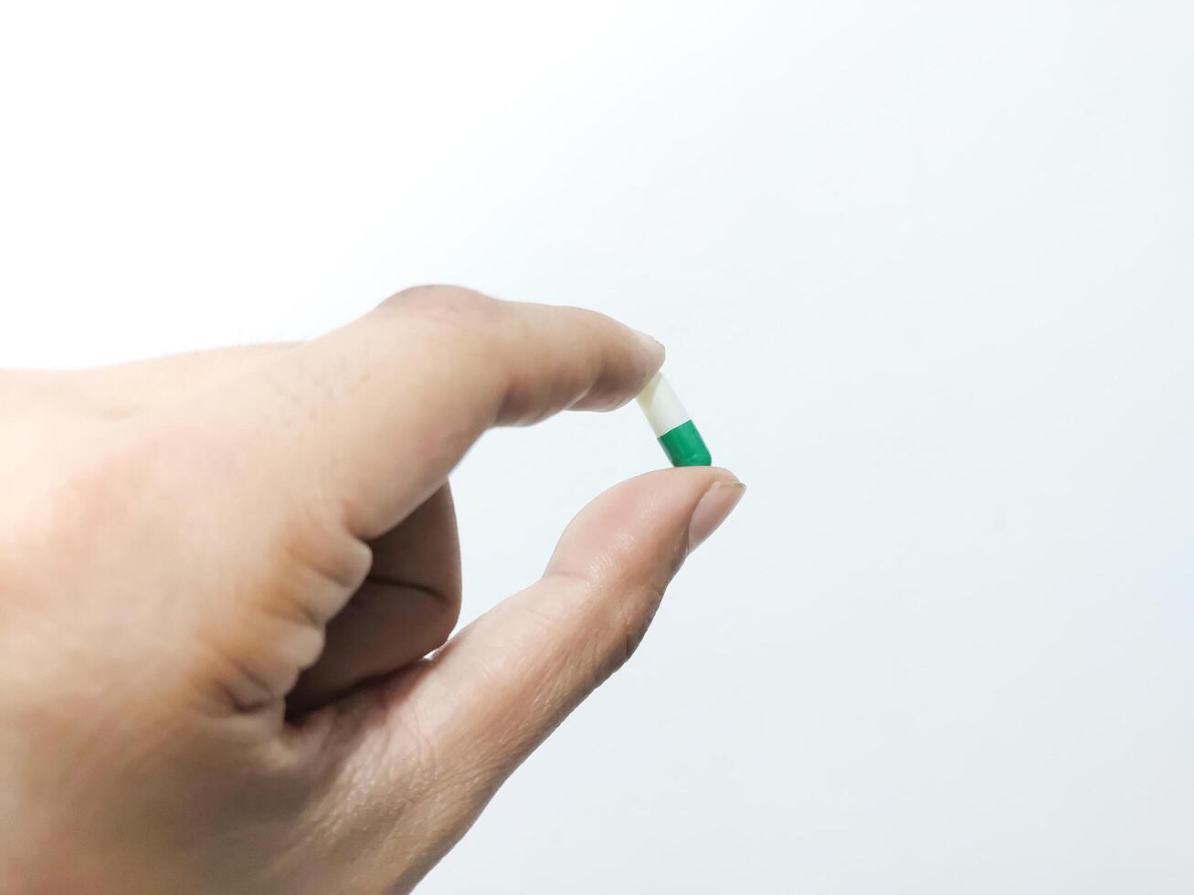 Fingers of a hand holding a capsule pill isolated on a white background photo