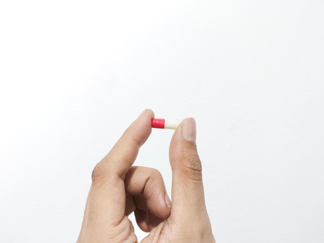 Fingers of a hand holding a capsule pill isolated on a white background photo