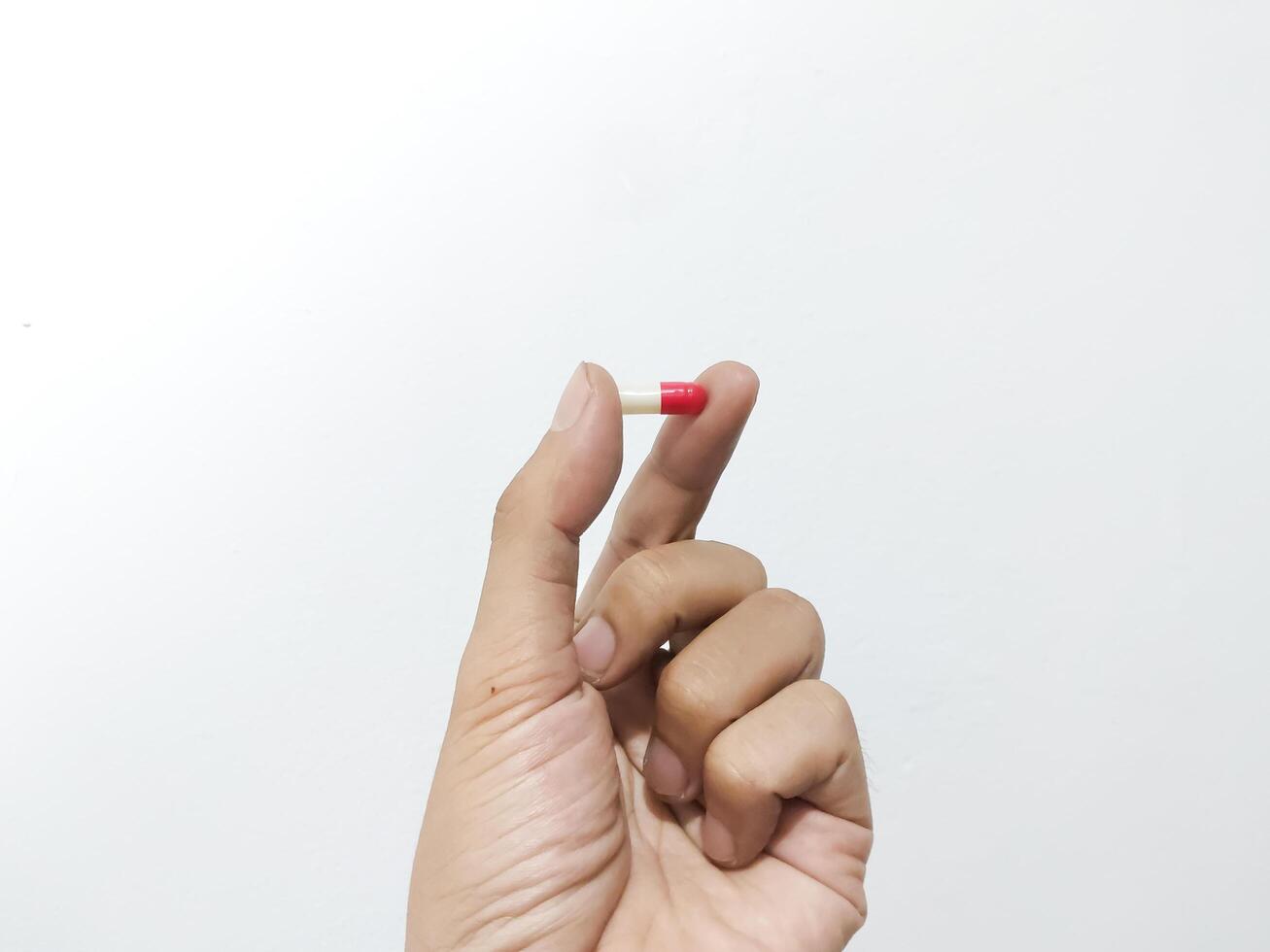 Fingers of a hand holding a capsule pill isolated on a white background photo