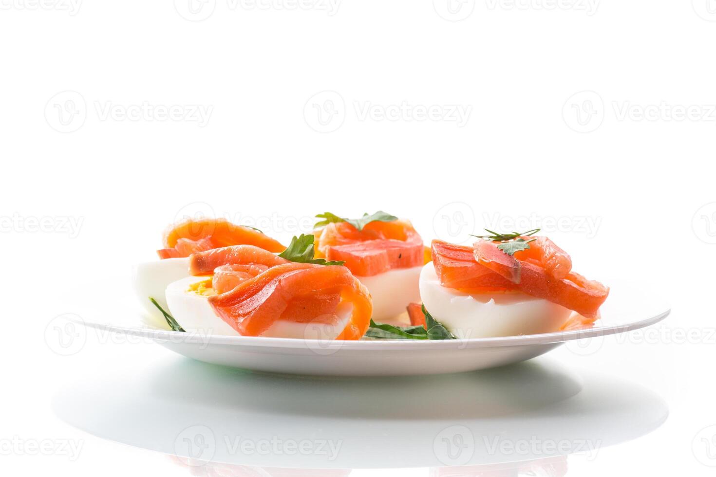 halves of boiled eggs with pieces of salted salmon on white background photo