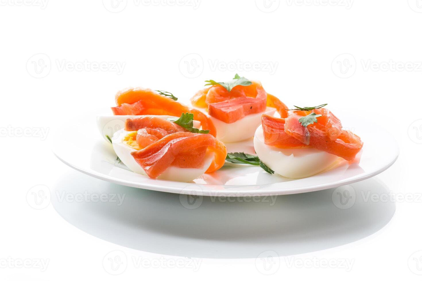 halves of boiled eggs with pieces of salted salmon on white background photo