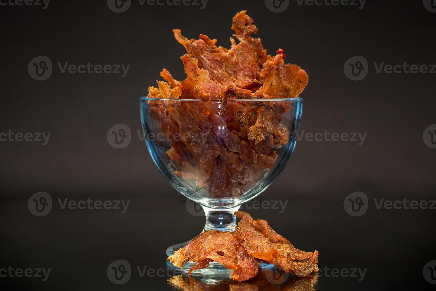 dried meat with spices in a glass bowl, isolated on black background photo