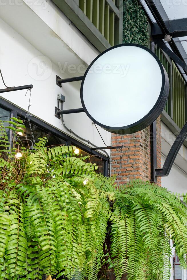 Blank round shop sign light box hanging on retro cafe with plant leaves photo