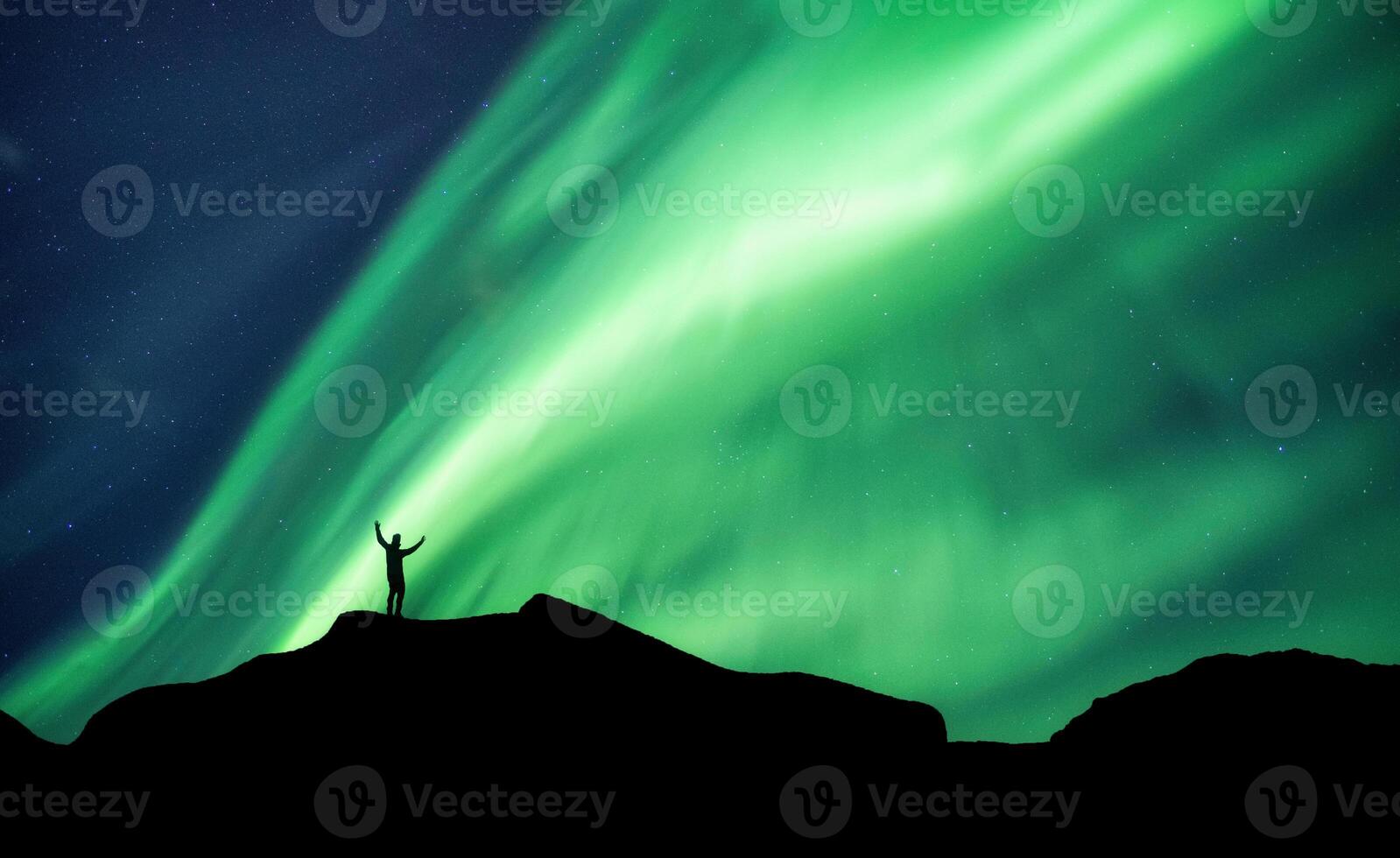 Mountaineer standing on top of mountain with Aurora Borealis glowing in the night sky on arctic circle photo