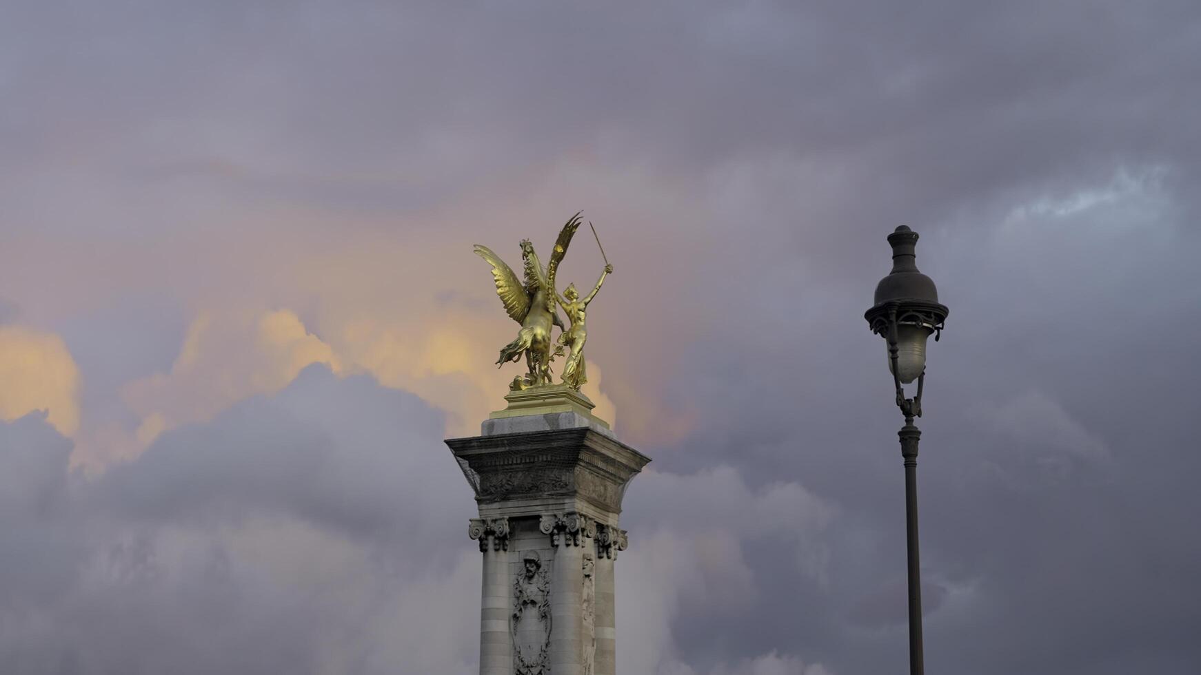 France, Paris - July 24, 2022. Golden statue on tower on background of clouds. Action. Beautiful landscape with golden sculpture on background of colorful evening clouds. Golden Statue of Alexander photo