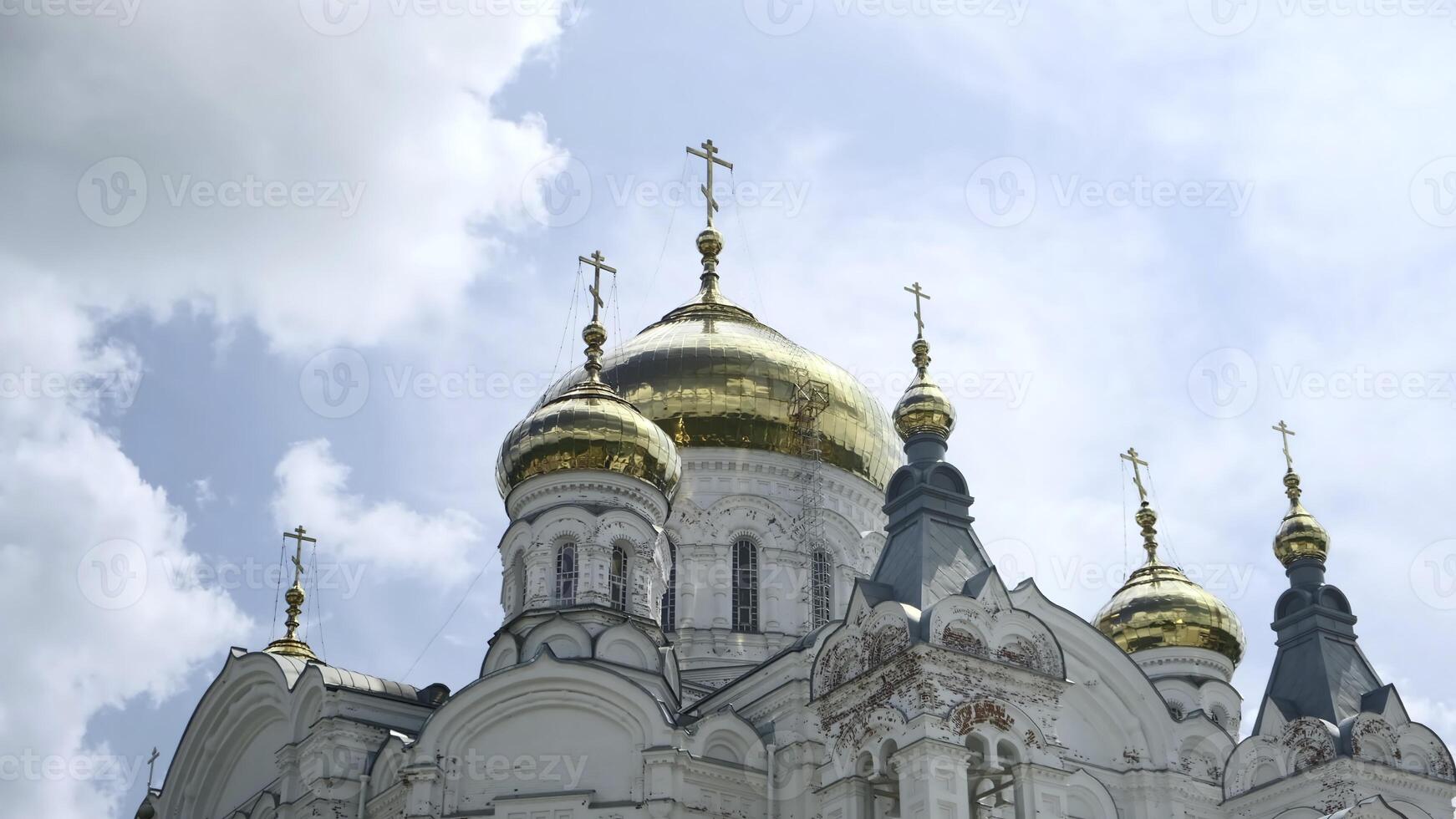 Picturesque view of Orthodox church. Clip. Beautiful white church with golden domes on background of blue sky in summer. Bottom view of historic white church with golden domes on sunny day photo