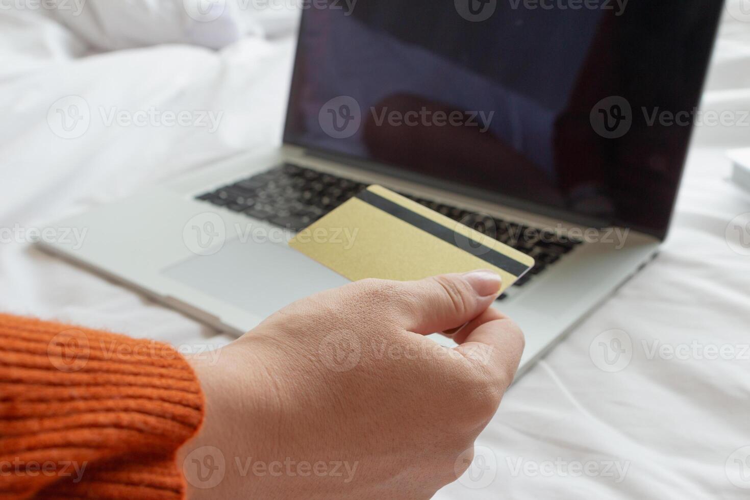 mujer sentado en su habitación es felizmente compras para regalos en línea con su crédito tarjeta como ella prepara para Navidad. mujer usos ordenador portátil a acceso un en línea compras sitio web y pagar con su crédito tarjeta. foto