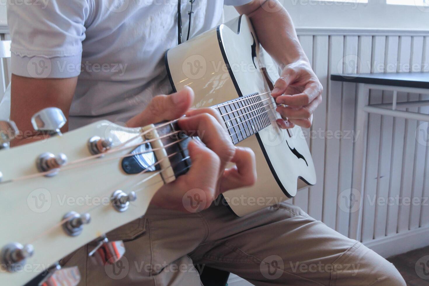 A young man is practicing playing guitar in a music practice room before performing in order to reduce the mistake of playing guitar on stage. Close Up Young man is holding guitar chords for practice. photo