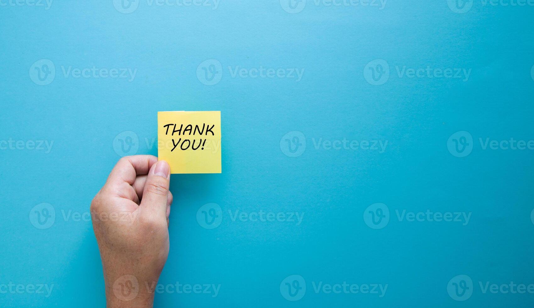 Male hand holds a yellow sticky note paper with the word thank you. photo