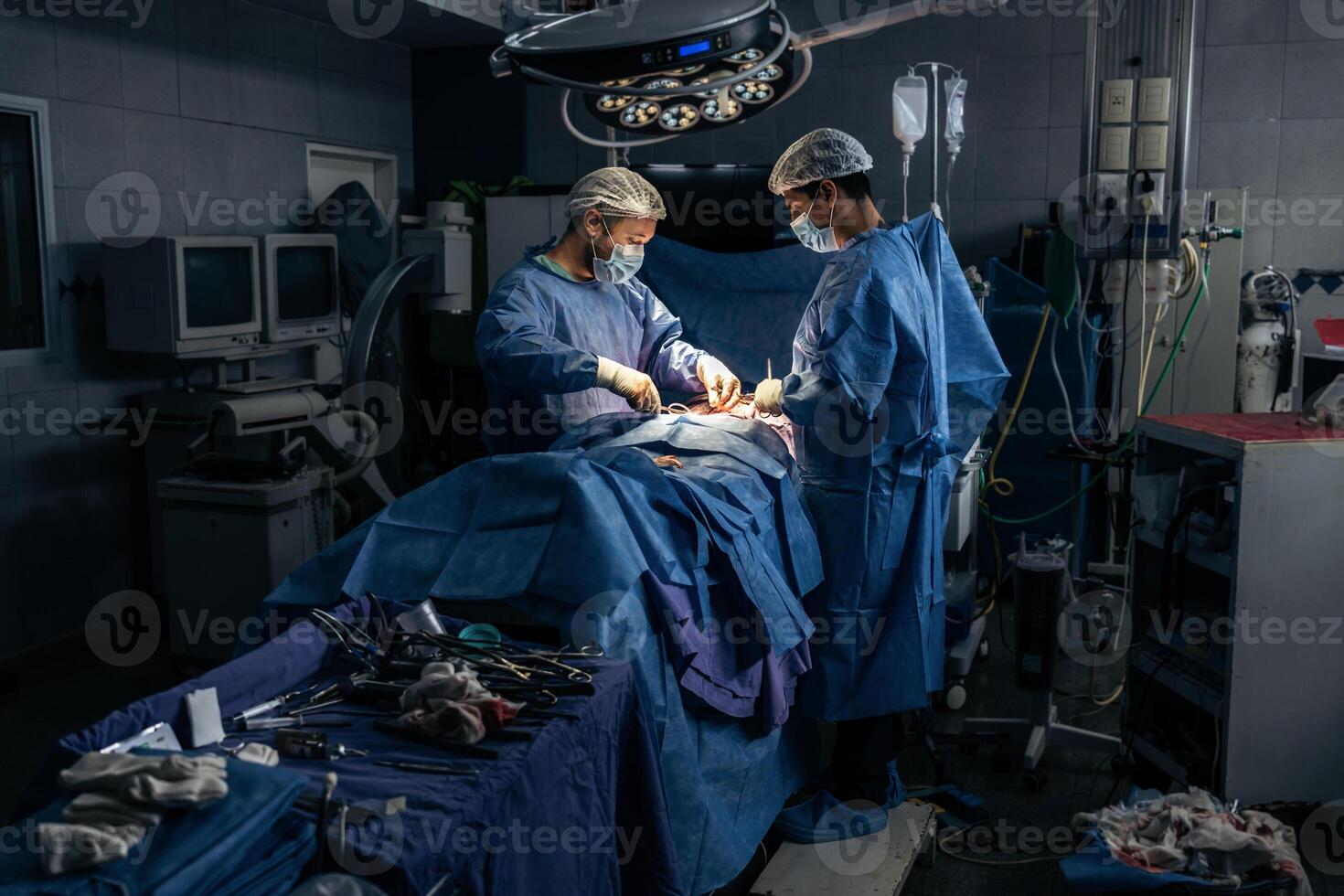 Wide view of a team of two surgeons operating on a patient in a dark OR at a hospital photo