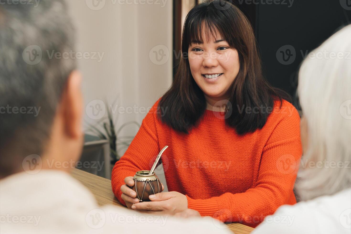 An Asian woman in a red sweater enjoys mate while chatting with two people. photo