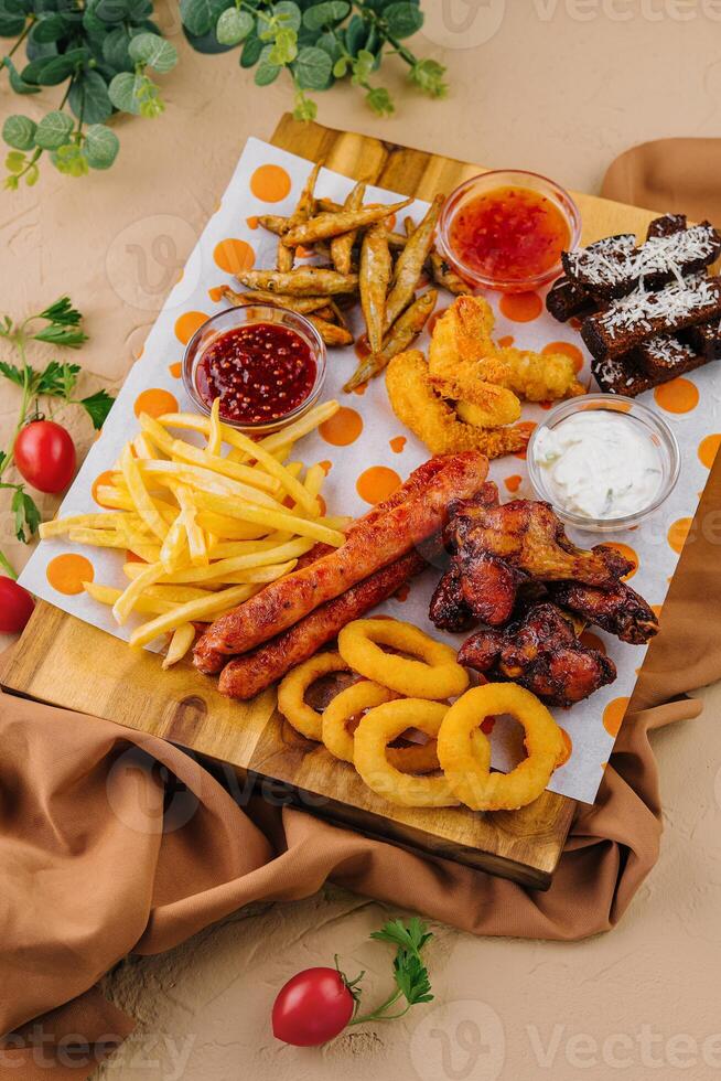 francés papas fritas patatas con cebolla anillos, salchichas, picatostes y picante pollo piernas foto