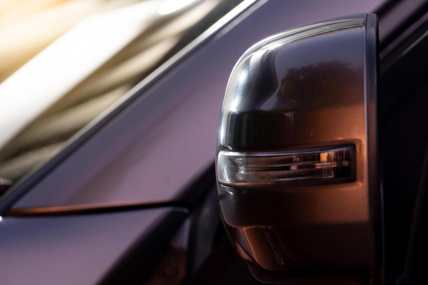 Beside view of mirror wing of car inclouds lamp of turn light. Warm evening light hits the gray car paint. photo