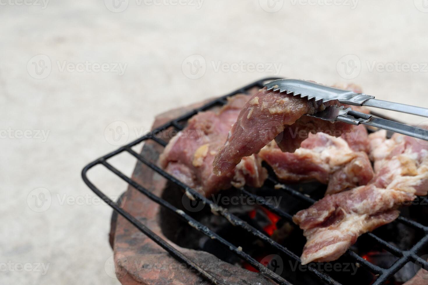 Pick up a piece of fresh pork with steel tongs. Three pieces of grilled pork on a rubber grill. Place on the charcoal stove. photo