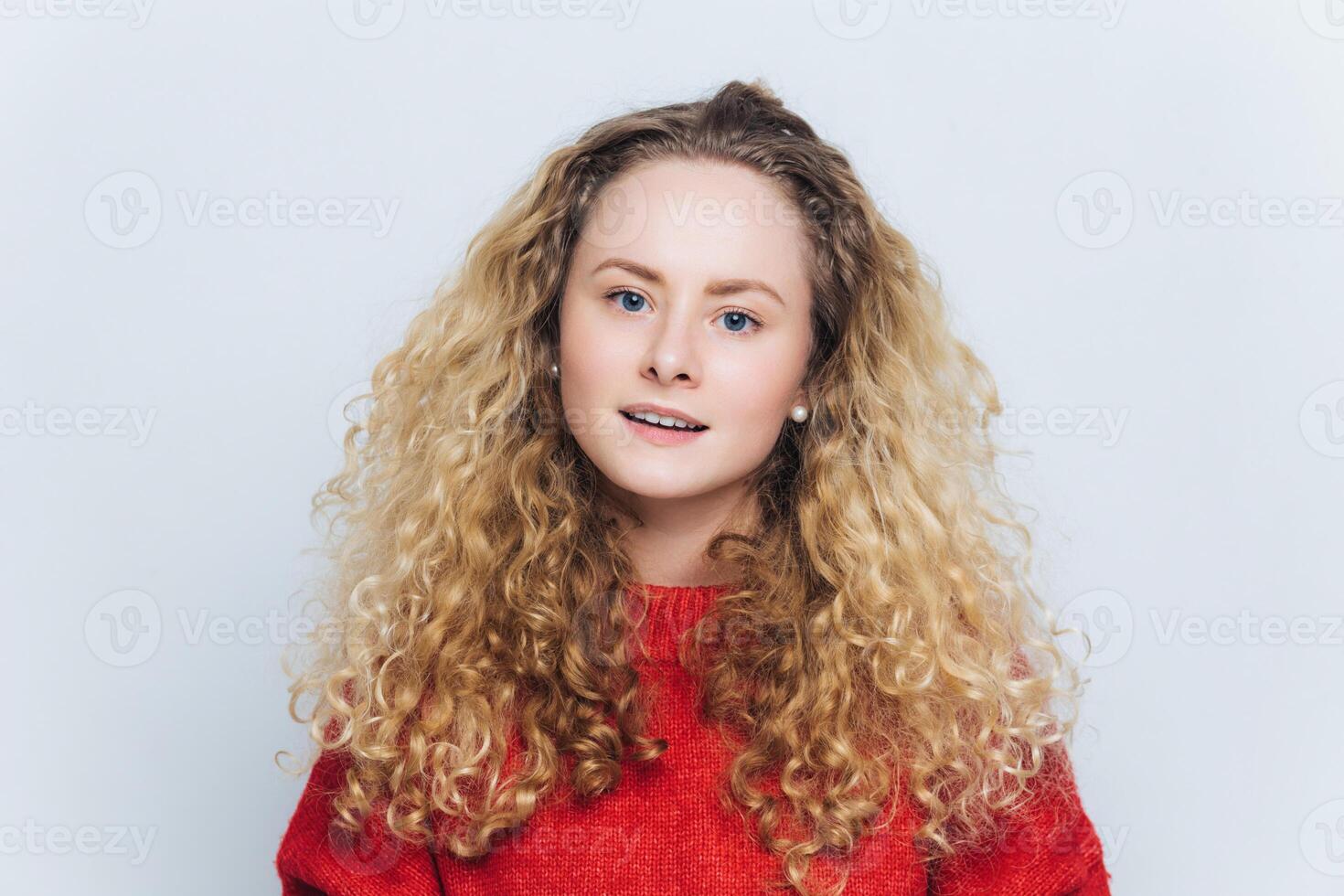 Vivacious young woman with curly blonde hair in a warm red sweater, radiating joy and comfort photo