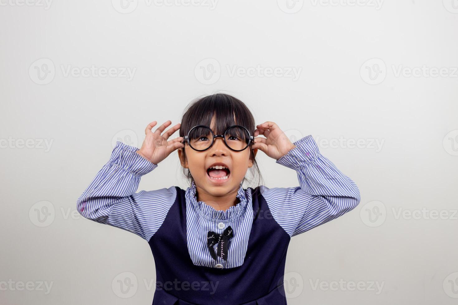 linda niñita en edad preescolar aislada en un estudio gris usa anteojos mira la cámara, un niño pequeño prueba anteojos en los ópticos, concepto de tratamiento de corrección de la vista para niños foto