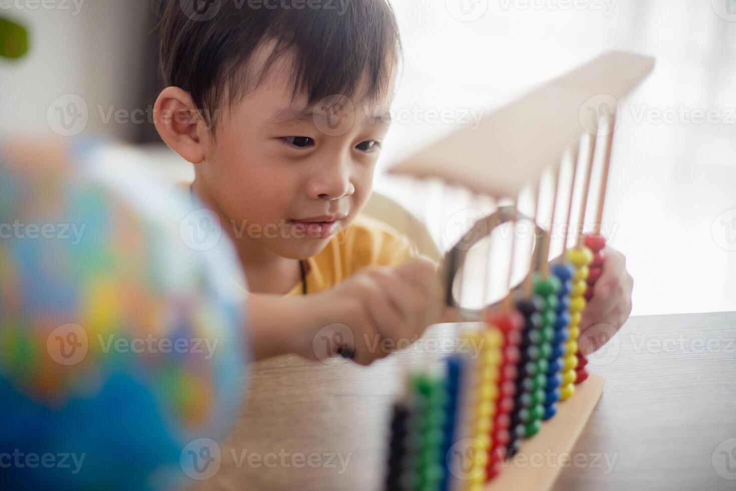 A young cute Asian boy is using the abacus with colored beads to learn how to count at home photo