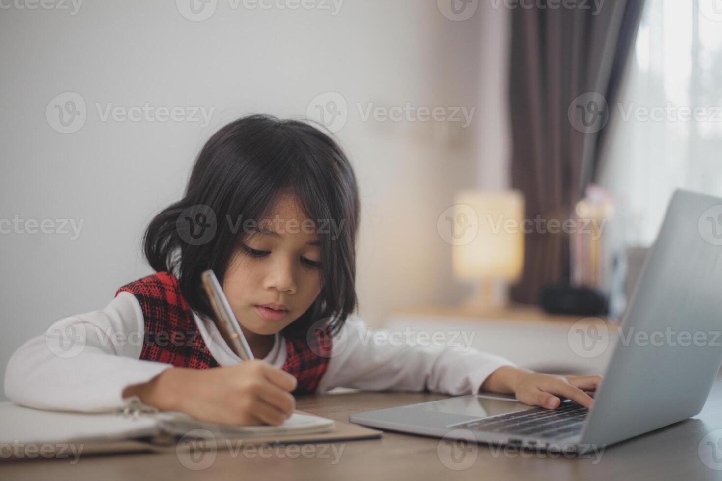 Cute and happy little Asian girl children using a laptop computer, studying through an online e-learning system at home. photo