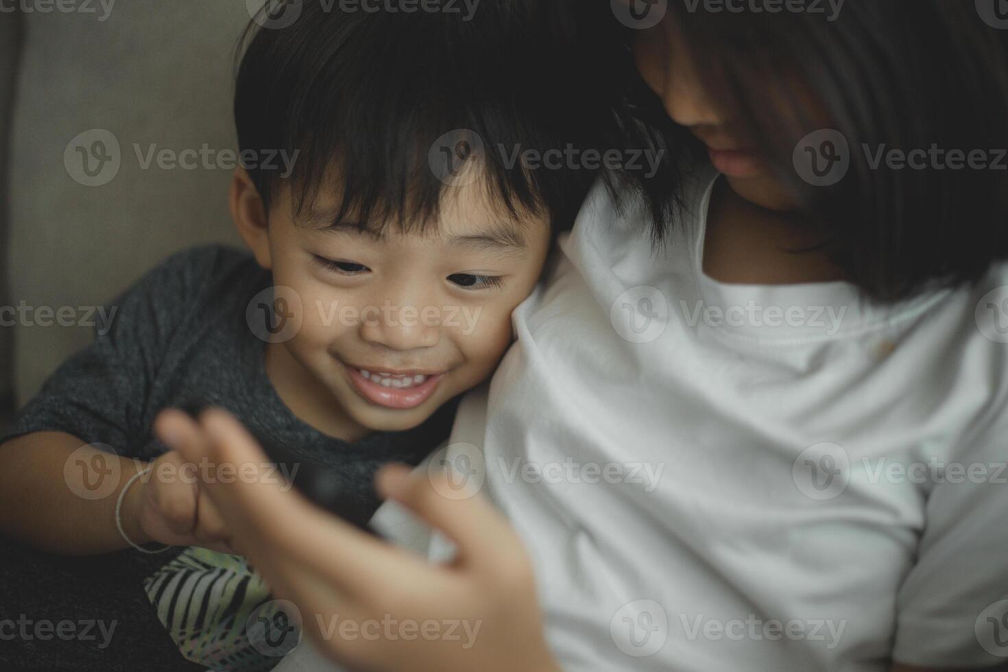 Little girls and boy siblings look at the phone and smile. They hold a smartphone watch videos, learn, play games, and speak online. Internet for children. Parental control photo