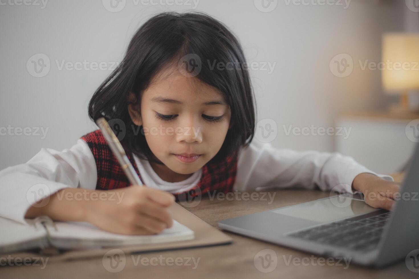 Cute and happy little Asian girl children using a laptop computer, studying through an online e-learning system at home. photo