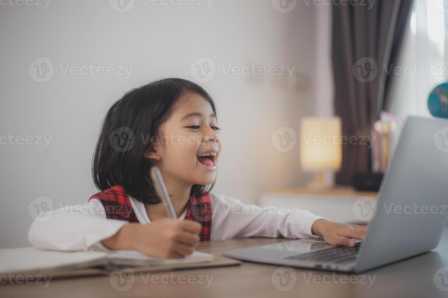 Cute and happy little Asian girl children using a laptop computer, studying through an online e-learning system at home. photo