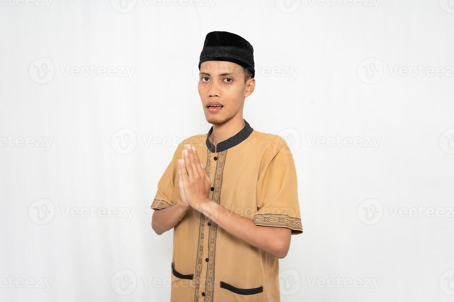 Asian Muslim man wearing brown Muslim clothes gives a greeting gesture to guests or friends. Isolated white background. photo