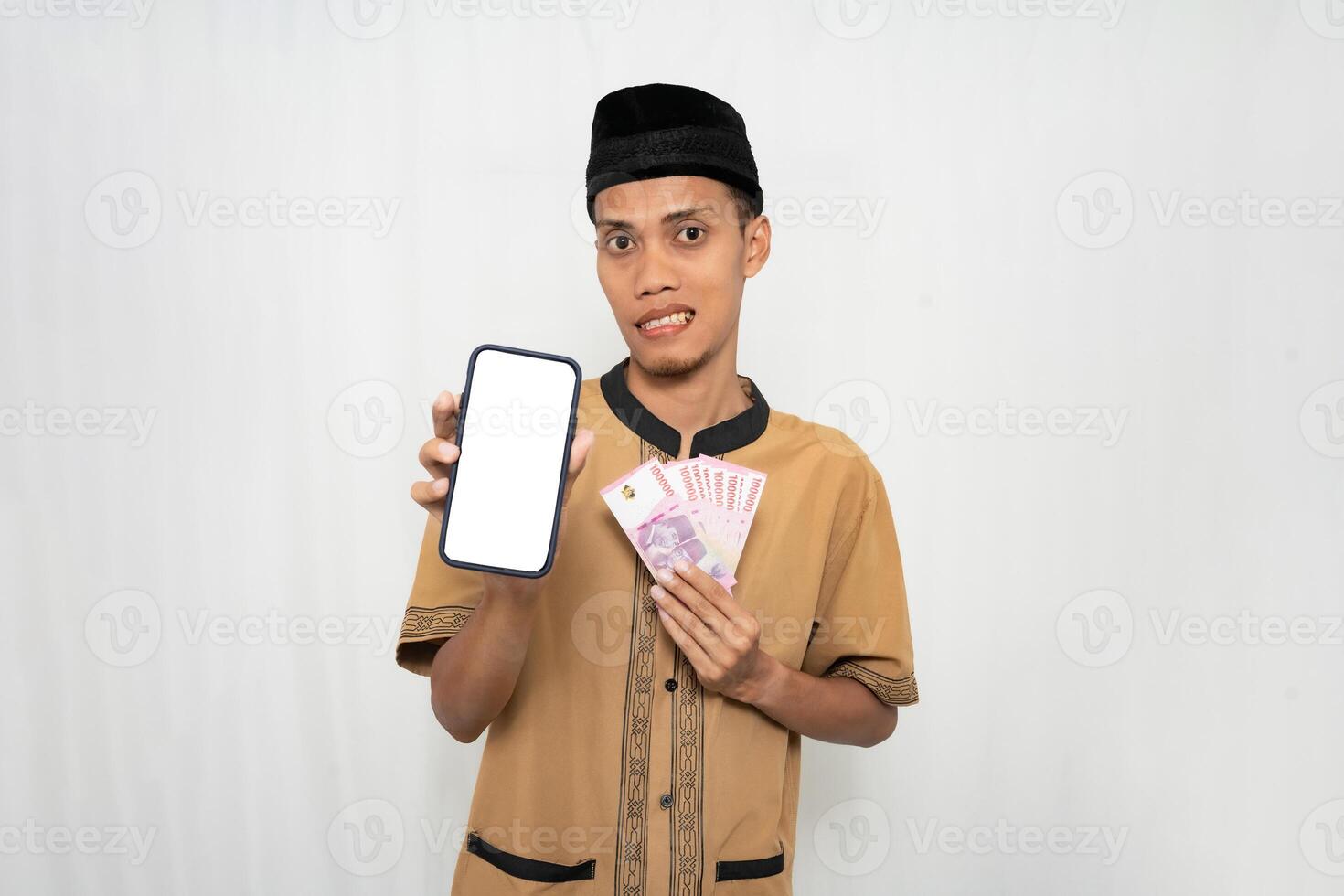 Asian Muslim man wearing brown Muslim clothes smiling happily while pointing at the smartphone screen. Isolated white background. photo