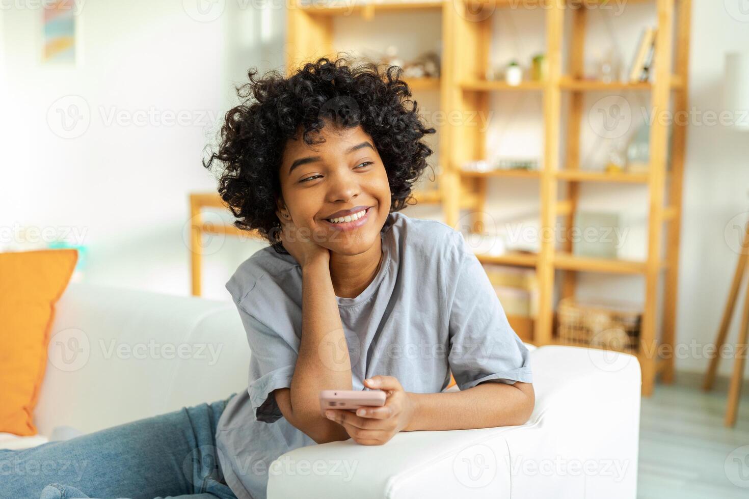 African girl holding smartphone touch screen typing scroll page at home. Woman with cell phone surfing internet using social media apps playing game. Shopping online Internet news cellphone addiction photo