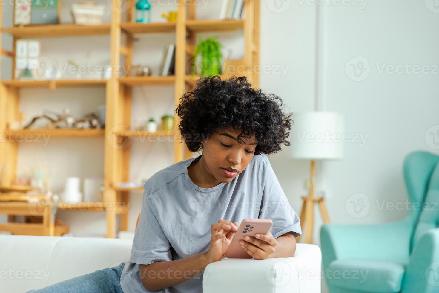 African girl holding smartphone touch screen typing scroll page at home. Woman with cell phone surfing internet using social media apps playing game. Shopping online Internet news cellphone addiction photo