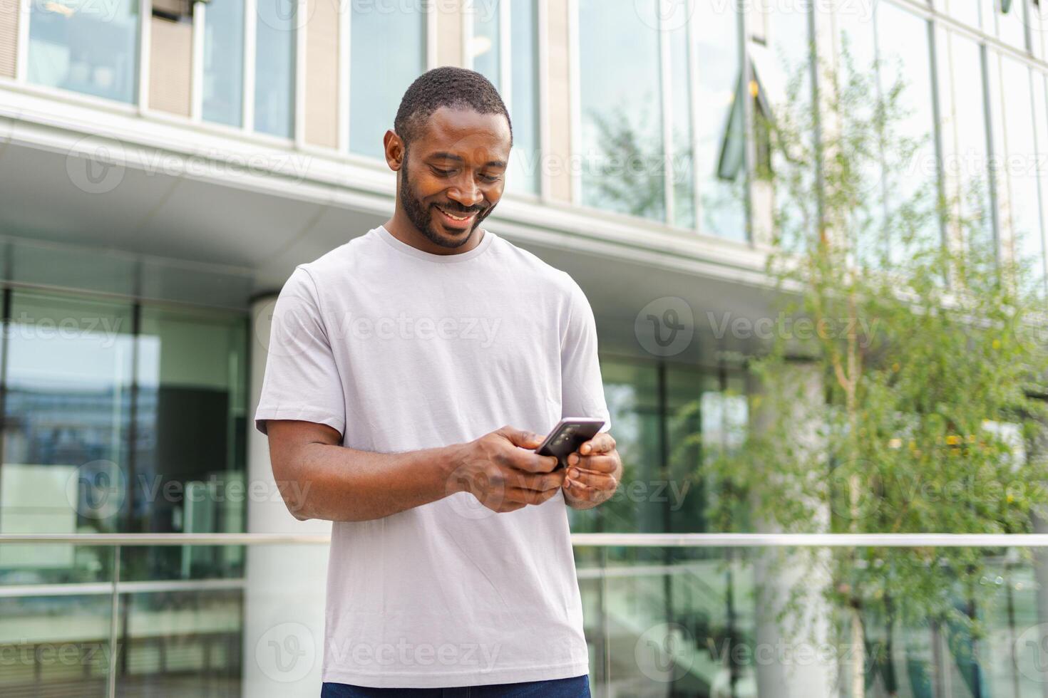 African american man holding smartphone touch screen typing scroll page on urban street in city. Guy with cell phone surfing internet using social media apps shopping online. Cellphone addiction photo