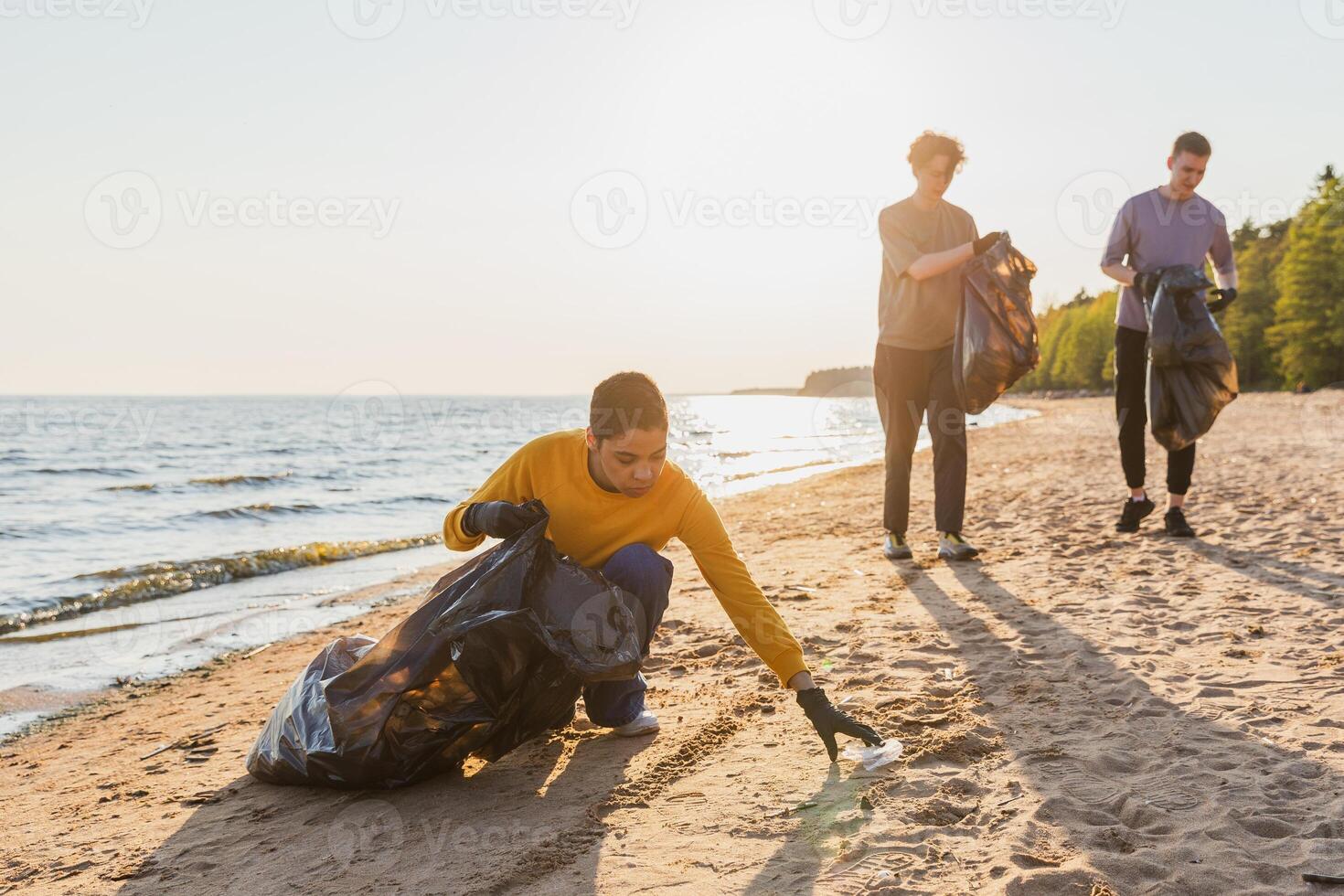 tierra día. voluntarios activistas equipo recoge basura limpieza de playa costero zona. mujer mans pone el plastico basura en basura bolso en Oceano costa. ambiental conservación costero zona limpieza foto