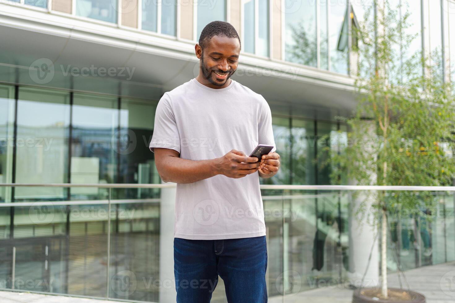 African american man holding smartphone touch screen typing scroll page on urban street in city. Guy with cell phone surfing internet using social media apps shopping online. Cellphone addiction photo