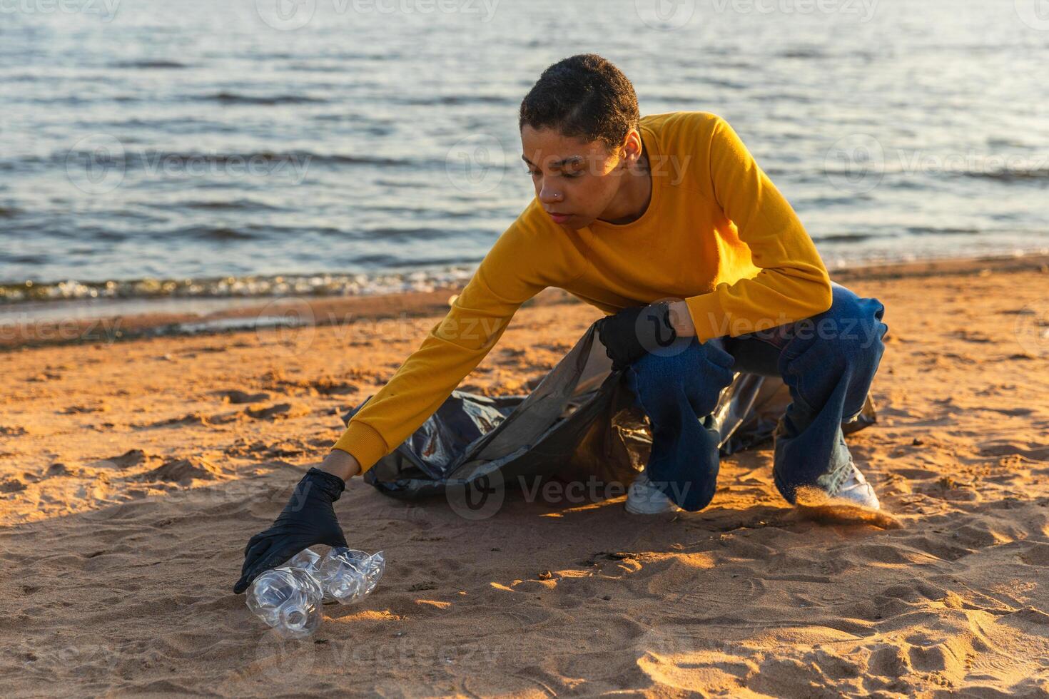 Earth day. Volunteers activists team collects garbage cleaning of beach coastal zone. Woman puts plastic trash in garbage bag on ocean shore. Environmental conservation coastal zone cleaning photo