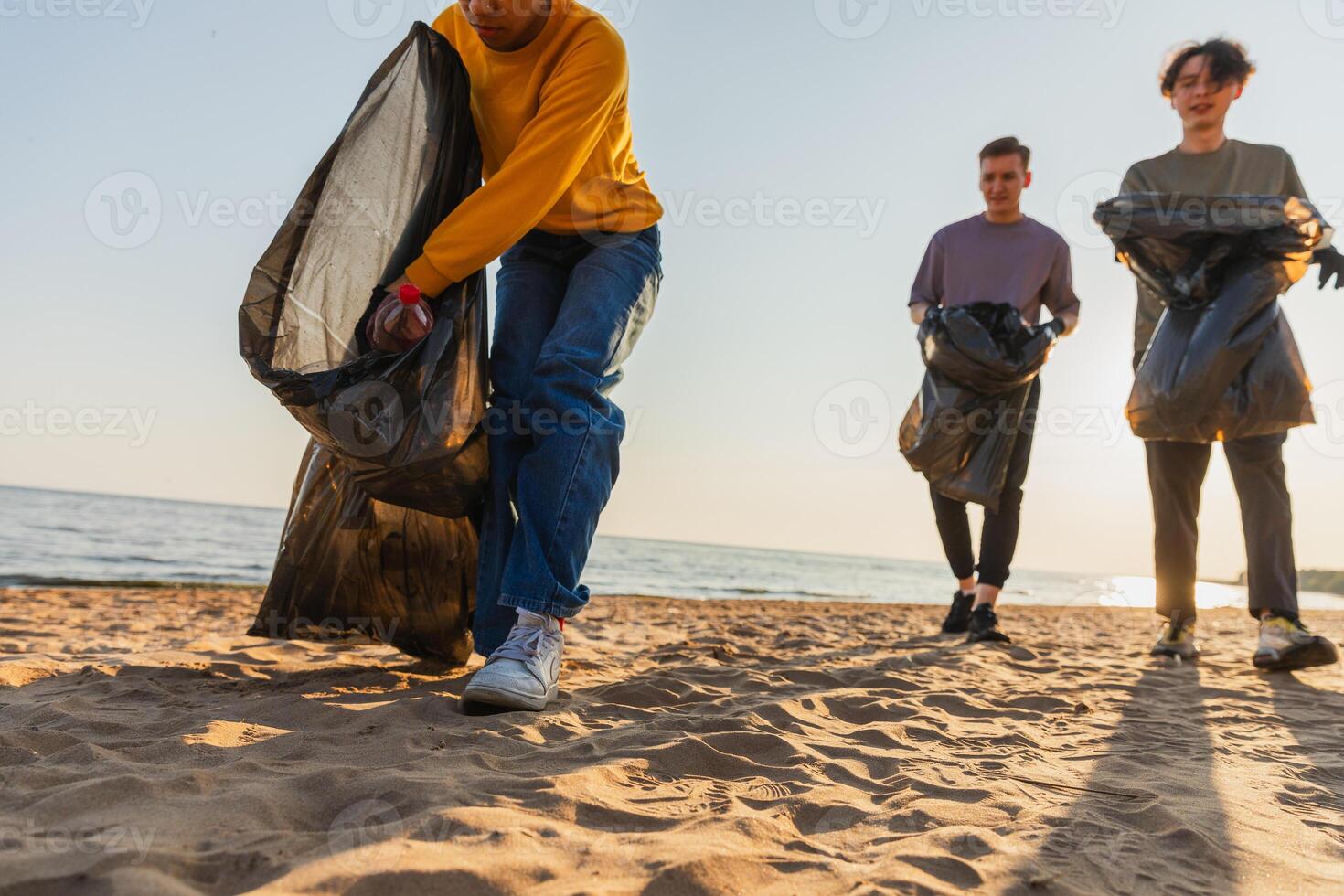 Earth day. Volunteers activists team collects garbage cleaning of beach coastal zone. Woman mans puts plastic trash in garbage bag on ocean shore. Environmental conservation coastal zone cleaning photo