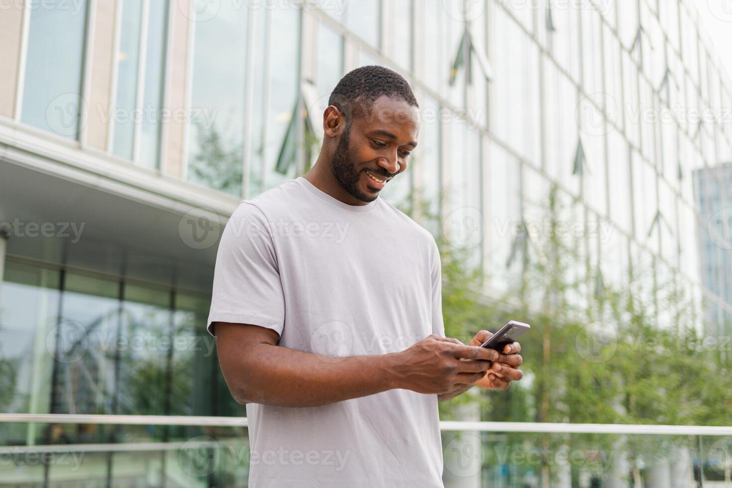 African american man holding smartphone touch screen typing scroll page on urban street in city. Guy with cell phone surfing internet using social media apps shopping online. Cellphone addiction photo