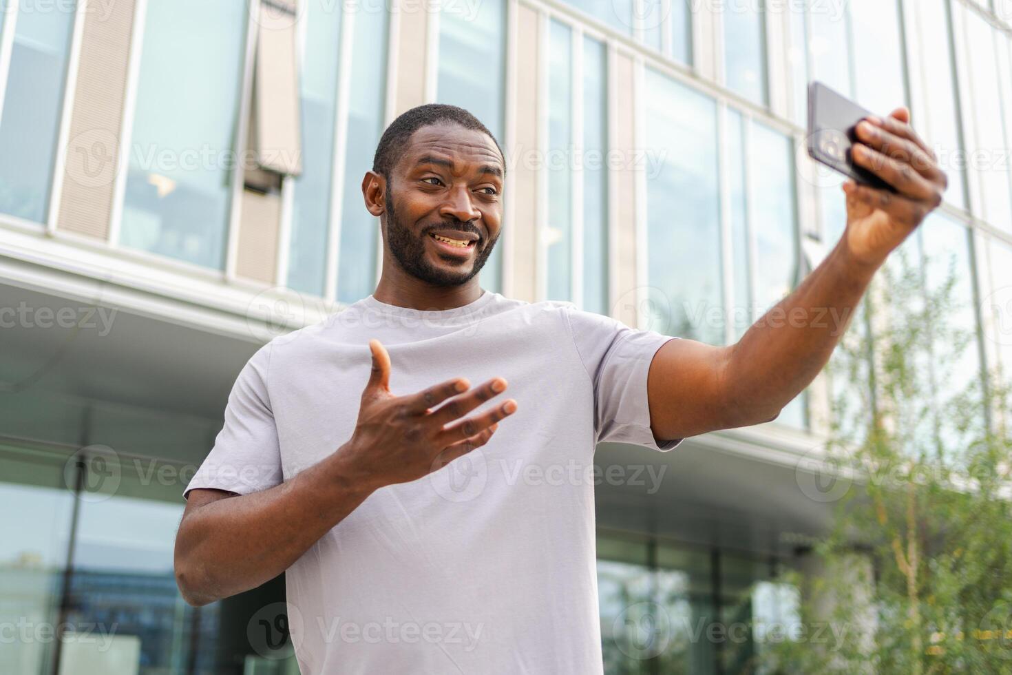 africano americano hombre participación teléfono inteligente teniendo vídeo charla en urbano calle en ciudad. chico blogger chateando con mejor amigos en social red. hombre teniendo virtual reunión en línea charla vídeo llamada al aire libre foto