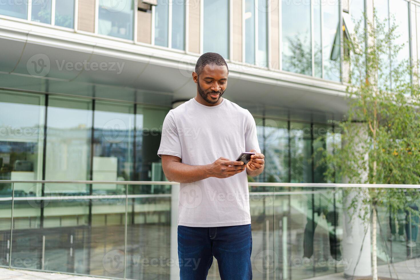 African american man holding smartphone touch screen typing scroll page on urban street in city. Guy with cell phone surfing internet using social media apps shopping online. Cellphone addiction photo