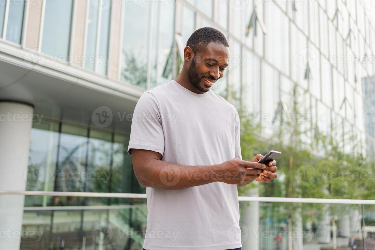 African american man holding smartphone touch screen typing scroll page on urban street in city. Guy with cell phone surfing internet using social media apps shopping online. Cellphone addiction photo