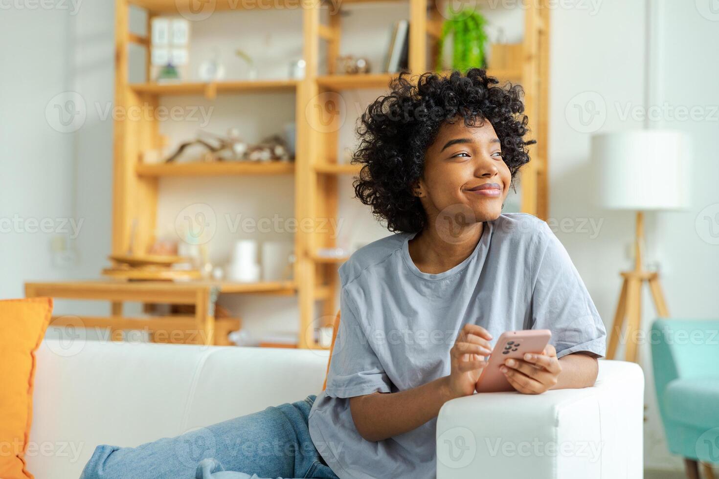 African girl holding smartphone touch screen typing scroll page at home. Woman with cell phone surfing internet using social media apps playing game. Shopping online Internet news cellphone addiction photo