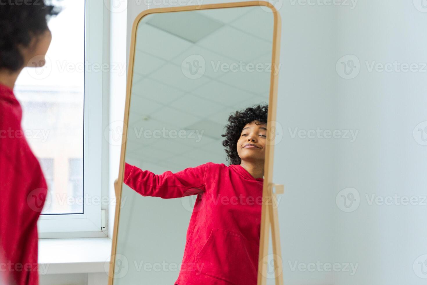 Love yourself. Beautiful young smiling african american woman dancing enjoying her mirror reflection. Black lady looking at mirror looking confident and happy. Self love concept photo