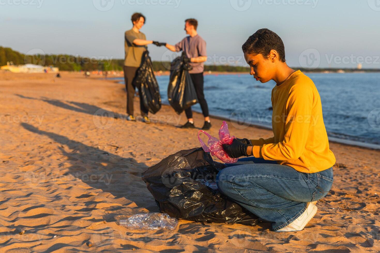 tierra día. voluntarios activistas equipo recoge basura limpieza de playa costero zona. mujer mans pone el plastico basura en basura bolso en Oceano costa. ambiental conservación costero zona limpieza foto