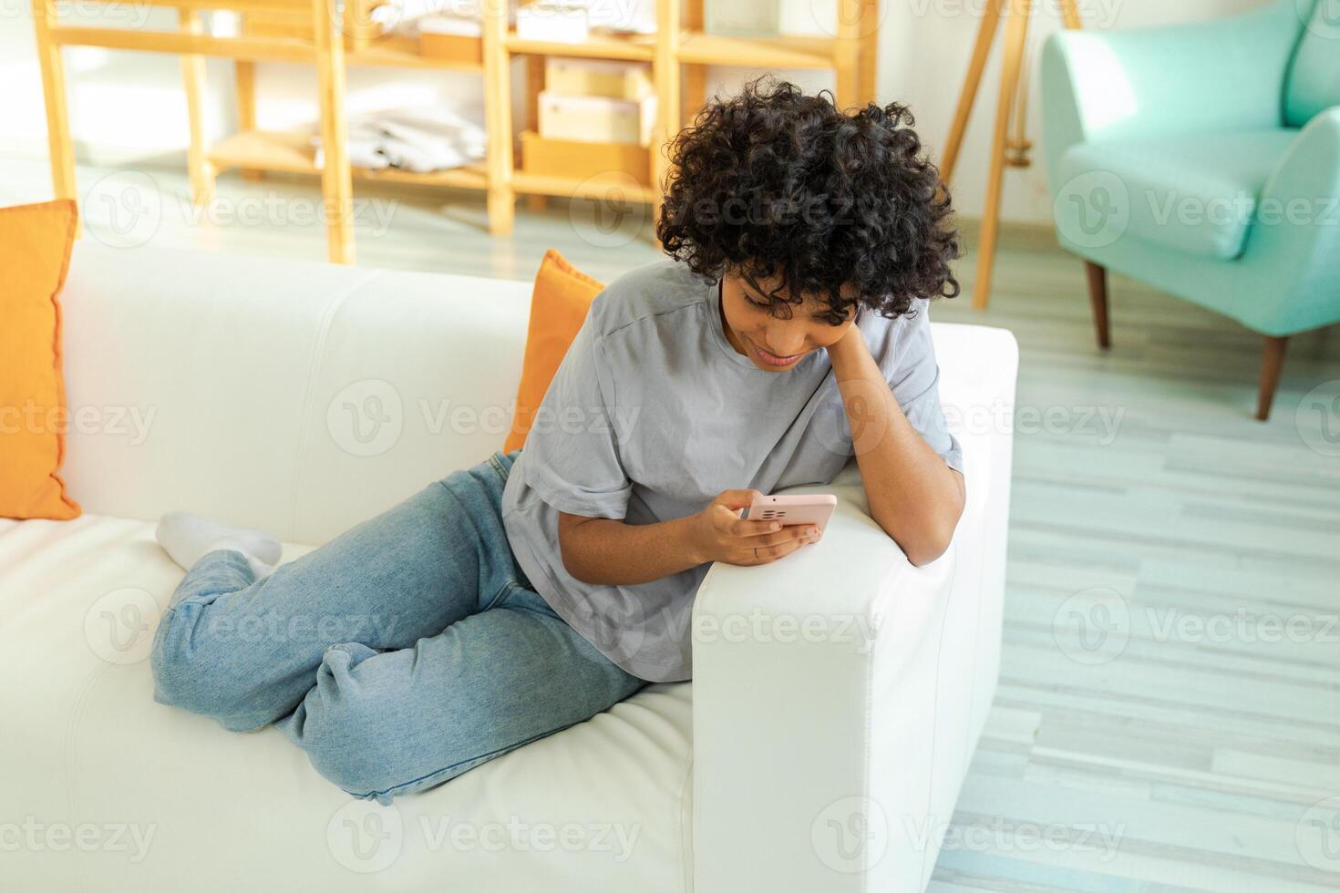 African girl holding smartphone touch screen typing scroll page at home. Woman with cell phone surfing internet using social media apps playing game. Shopping online Internet news cellphone addiction photo