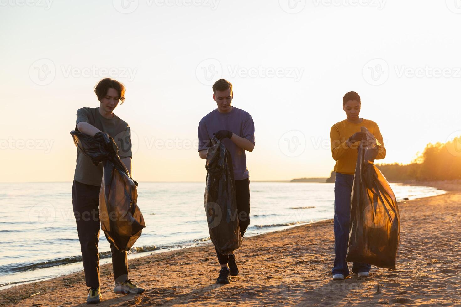 Earth day. Volunteers activists team collects garbage cleaning of beach coastal zone. Woman mans with trash in garbage bag on ocean shore. Environmental conservation coastal zone cleaning photo