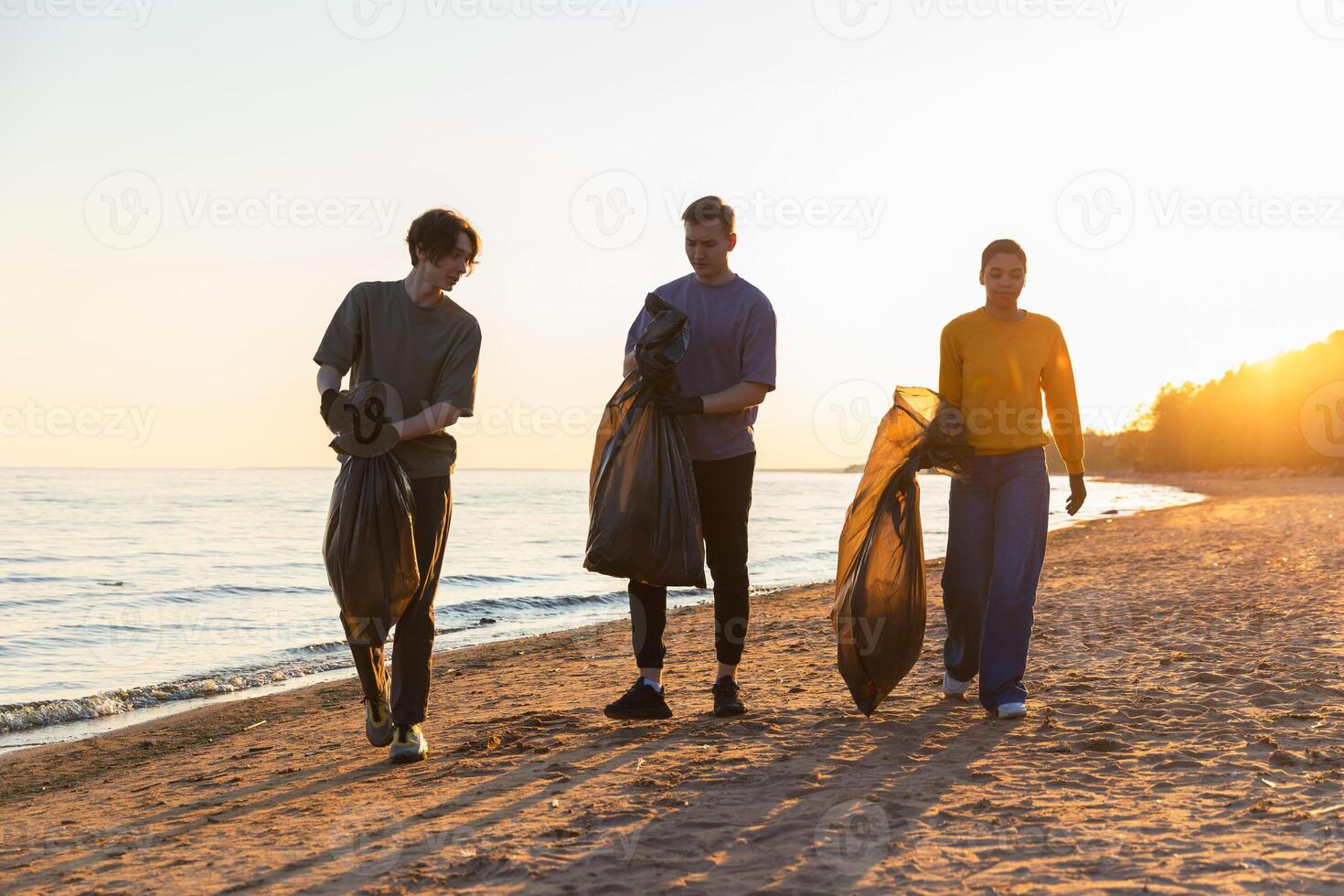 Earth day. Volunteers activists team collects garbage cleaning of beach coastal zone. Woman mans with trash in garbage bag on ocean shore. Environmental conservation coastal zone cleaning photo