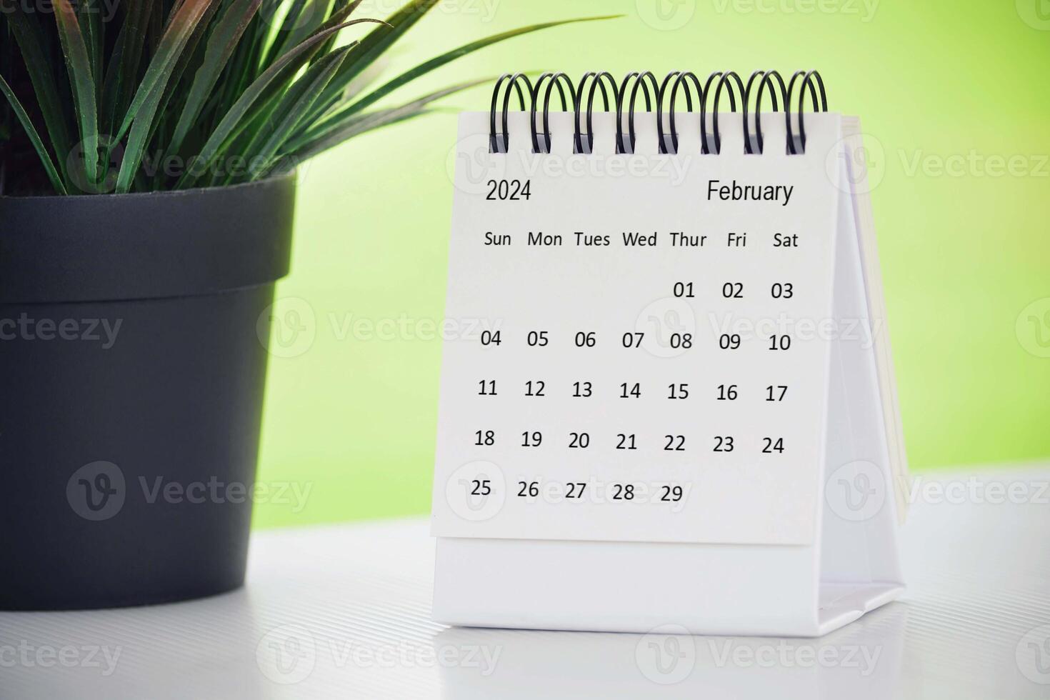 febrero 2024 escritorio calendario con en conserva planta en un escritorio con verde antecedentes. foto