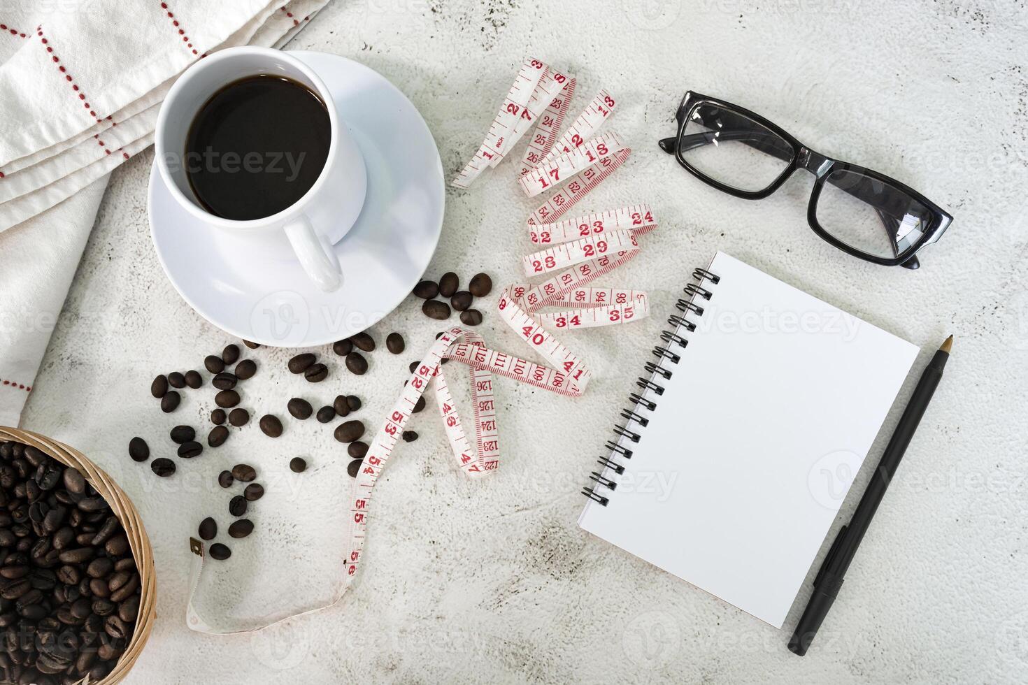 Cup of coffee and coffee beans background with measure tap and notebook. photo