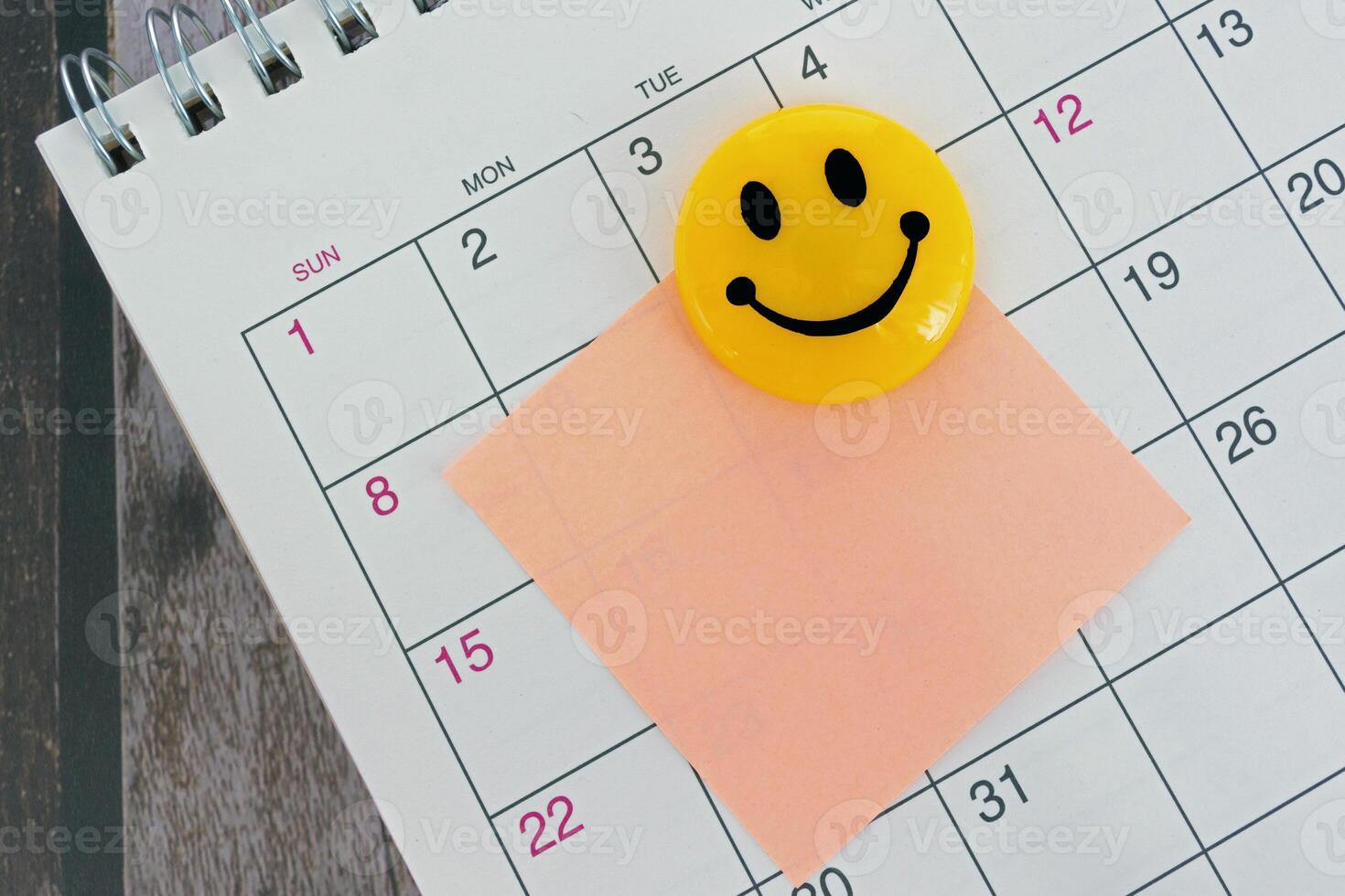 Orange paper sticky note with smiley face and stuck to a calendar background. photo