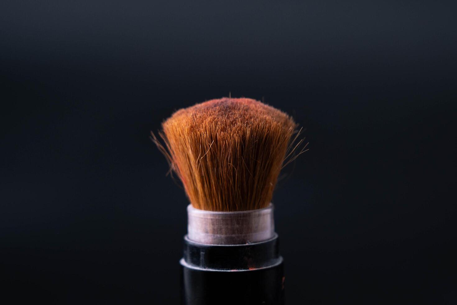 Cosmetic brush with pastel pink cosmetic powder spread on black background. Makeup brush with pink powder explosion close up. photo