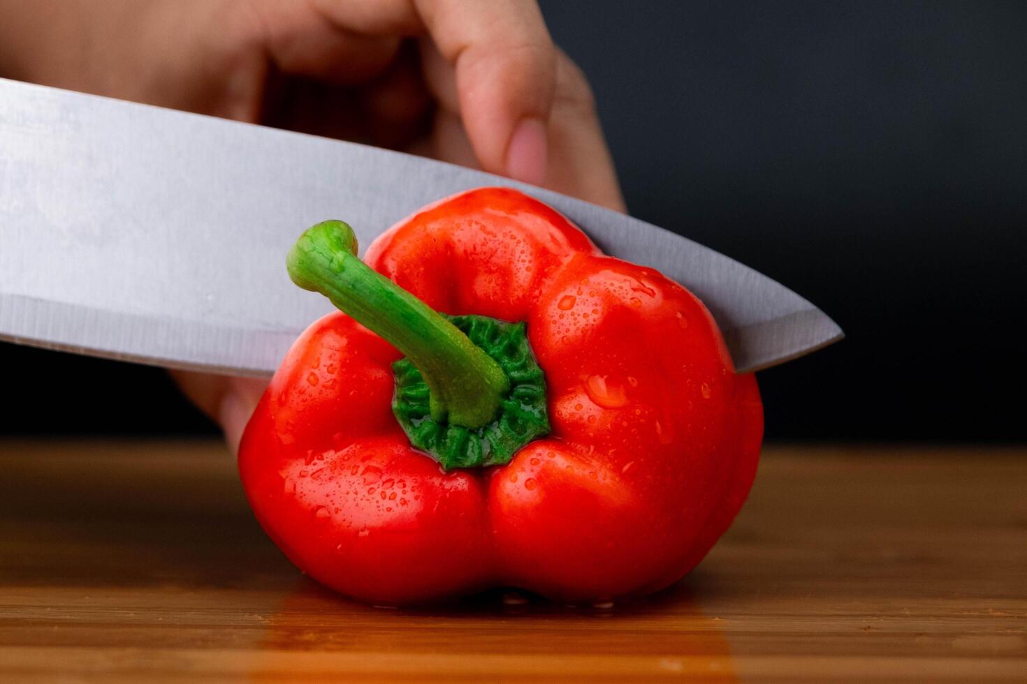 Hands cutting red bell peppers on a wooden chopping board. Woman chopping bell peppers in kitchen close up. photo