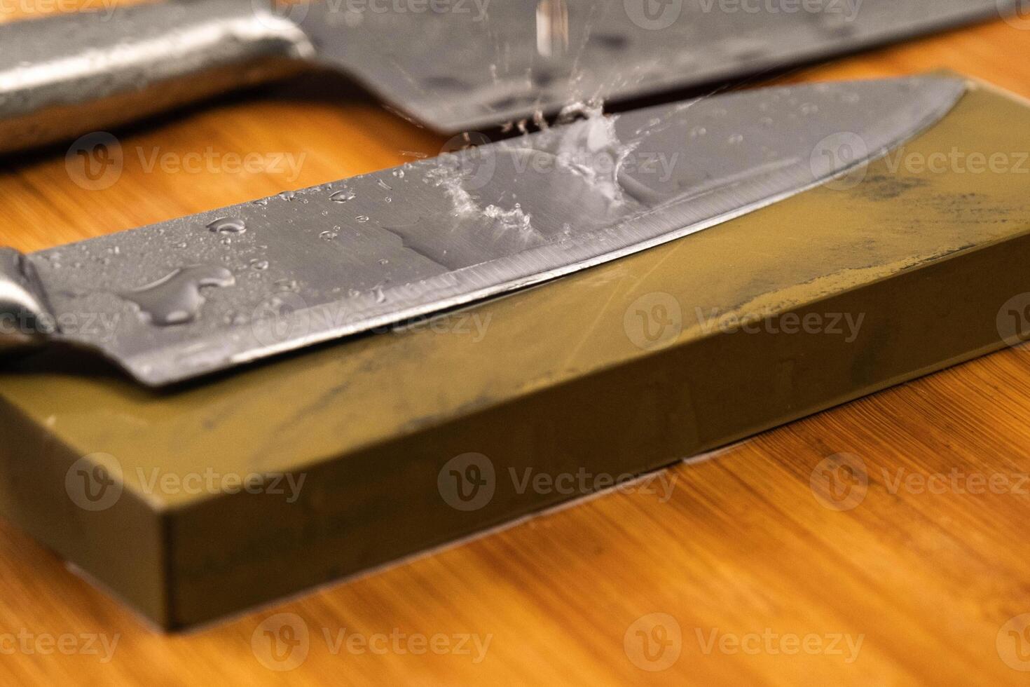 Sharpening knives with a Whetstone. Knife sharpening. Sharp knife and sharpening stone on a wooden cutting board. photo